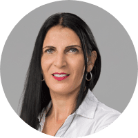 A professional headshot of Yasmin Aboudy, a woman with long dark hair, wearing earrings, a white shirt, and a confident smile.